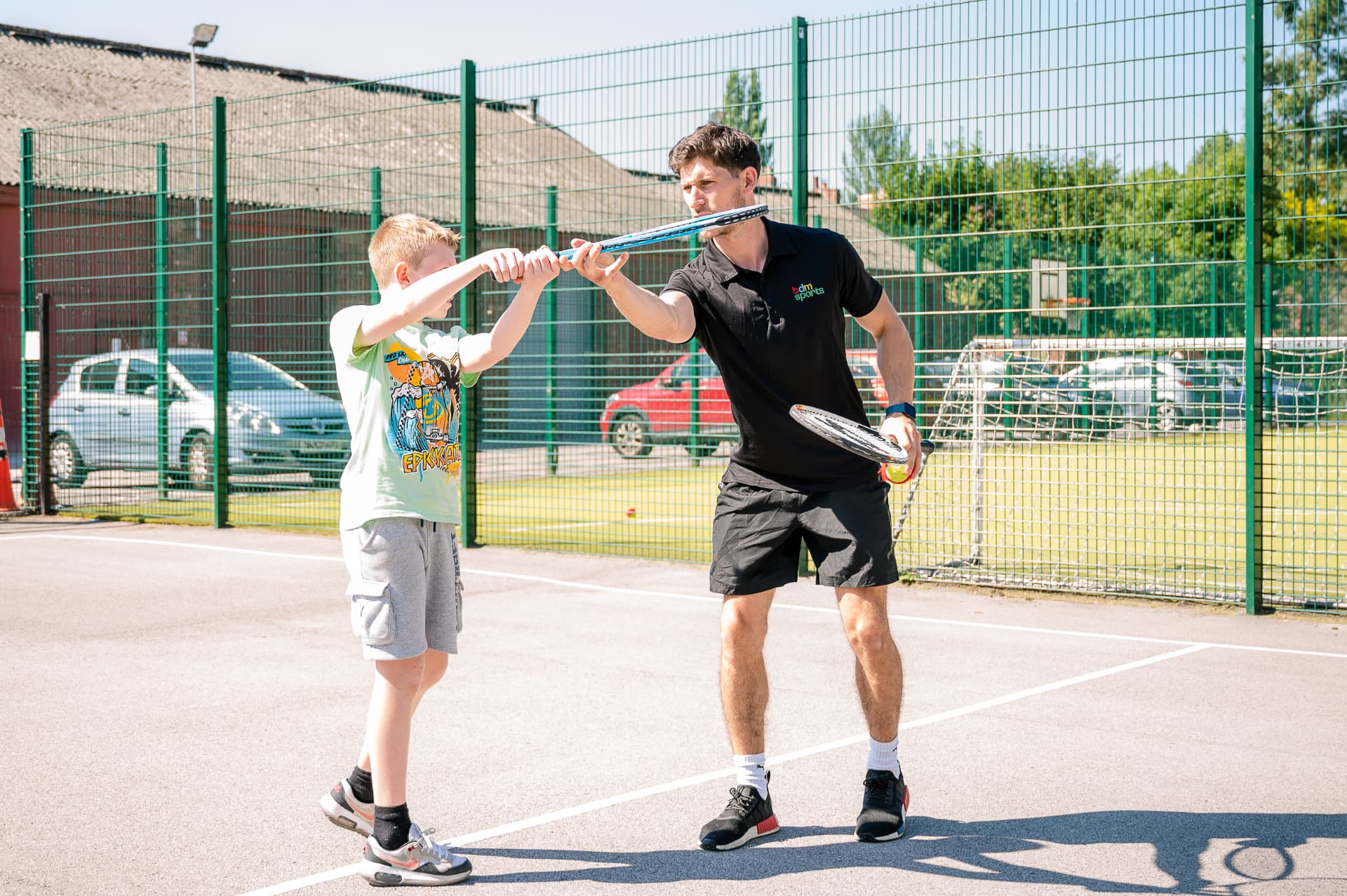 Coach guiding a boy's tennis racket on court